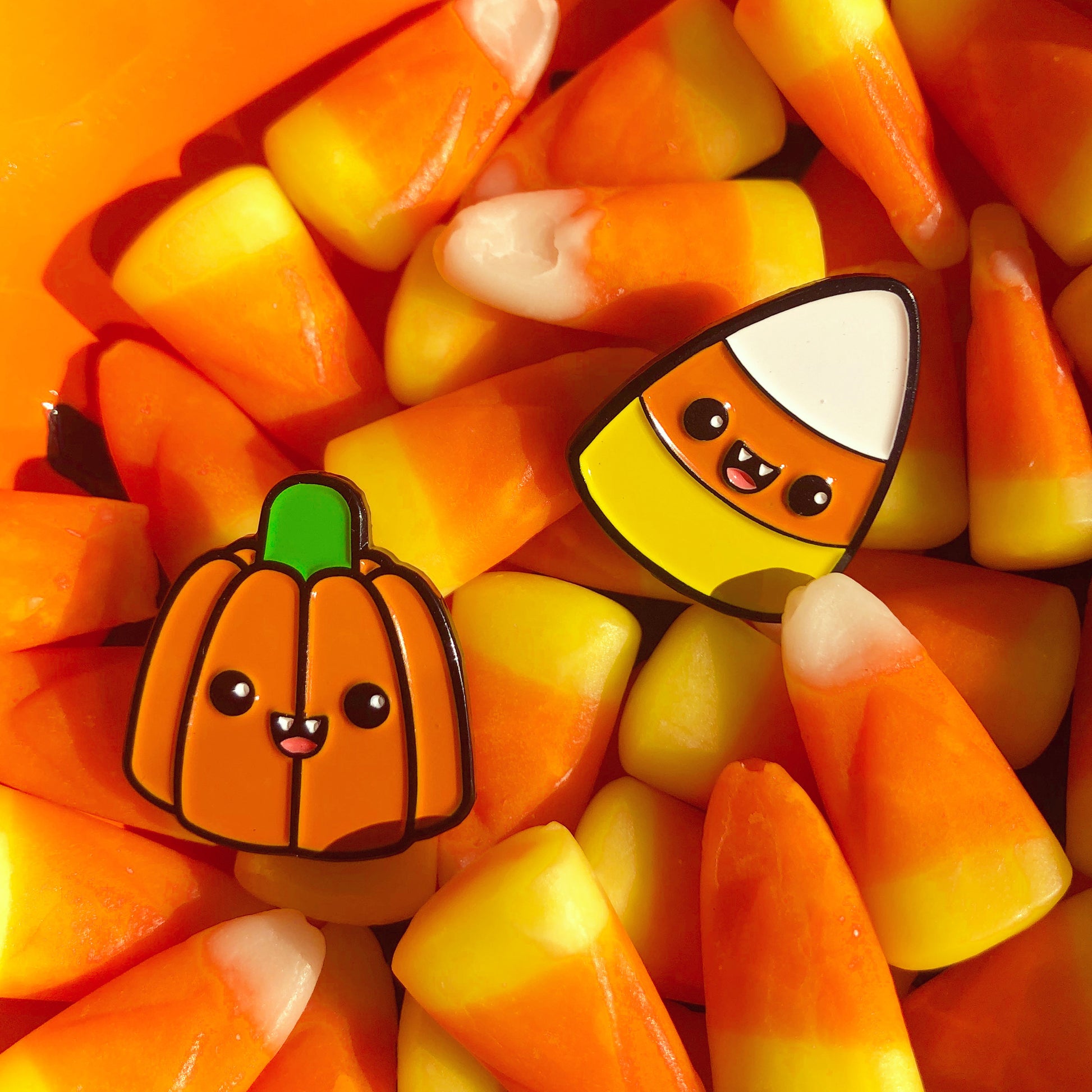 Halloween Pumpkin and Candy Corn enamel pin set laying on pile of candy corn