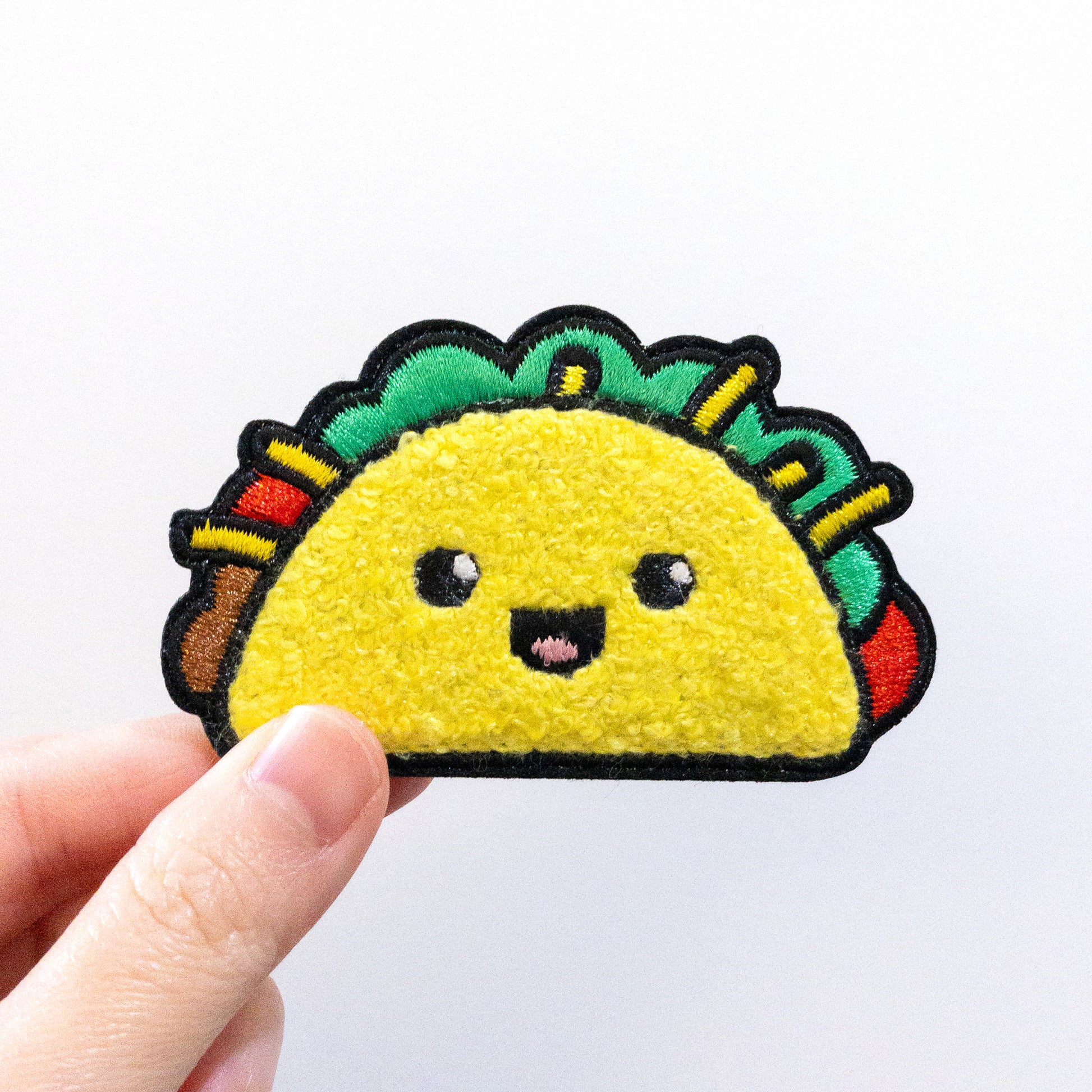 Hand holding a Taco iron on chenille patch