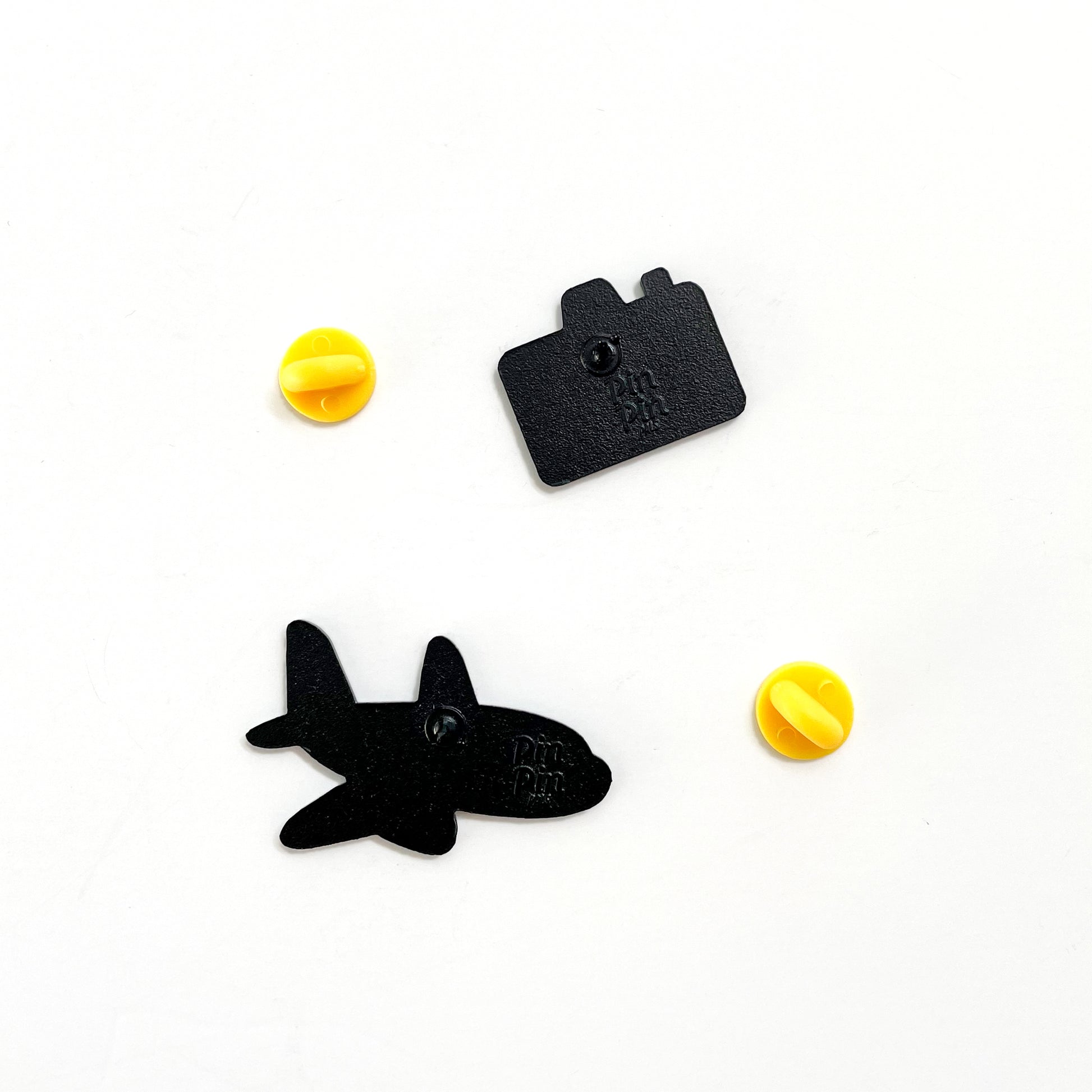 Back of plane and camera enamel pins with yellow rubber backings